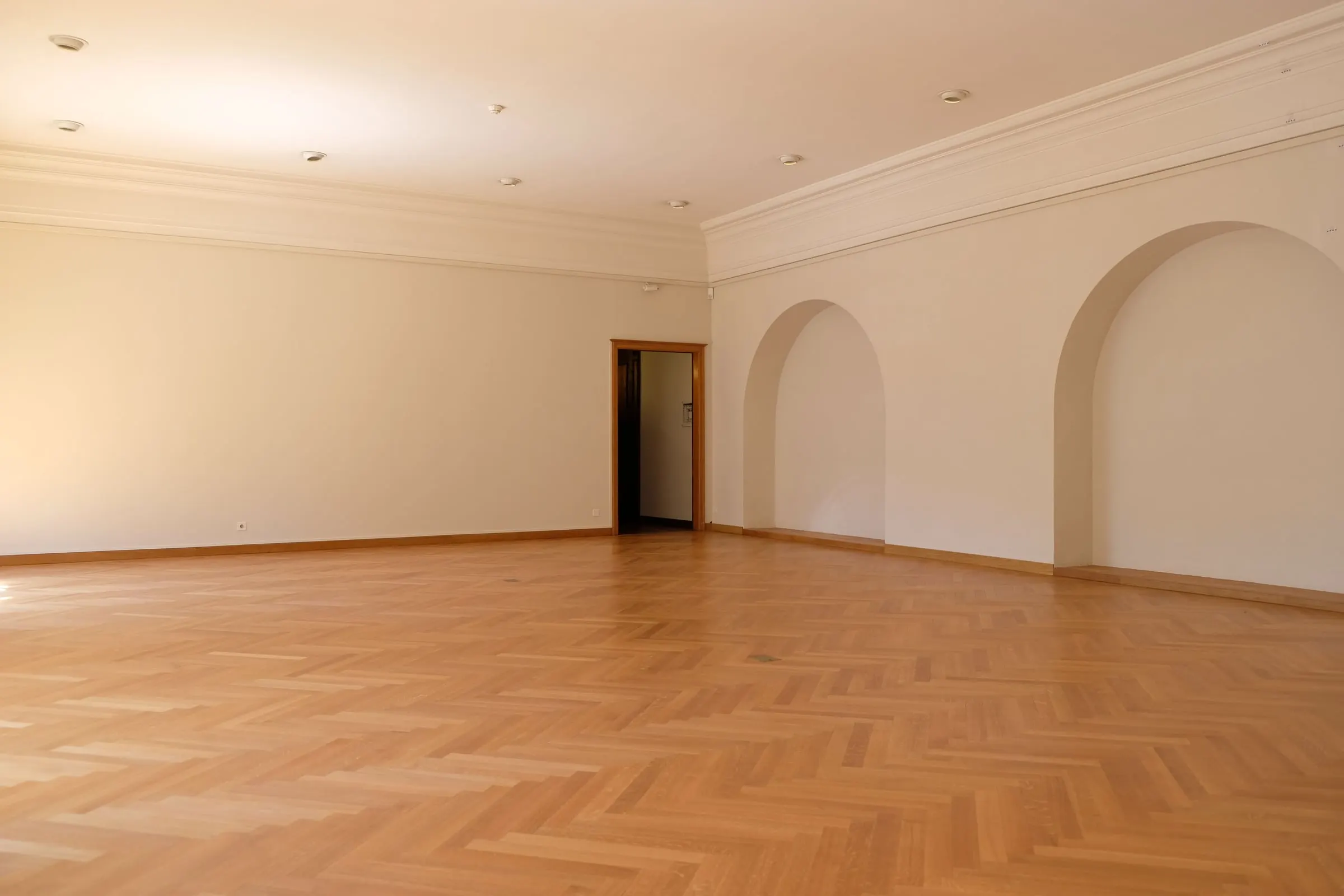 Large empty room with cream walls, arched alcoves and a timber herringbone floor